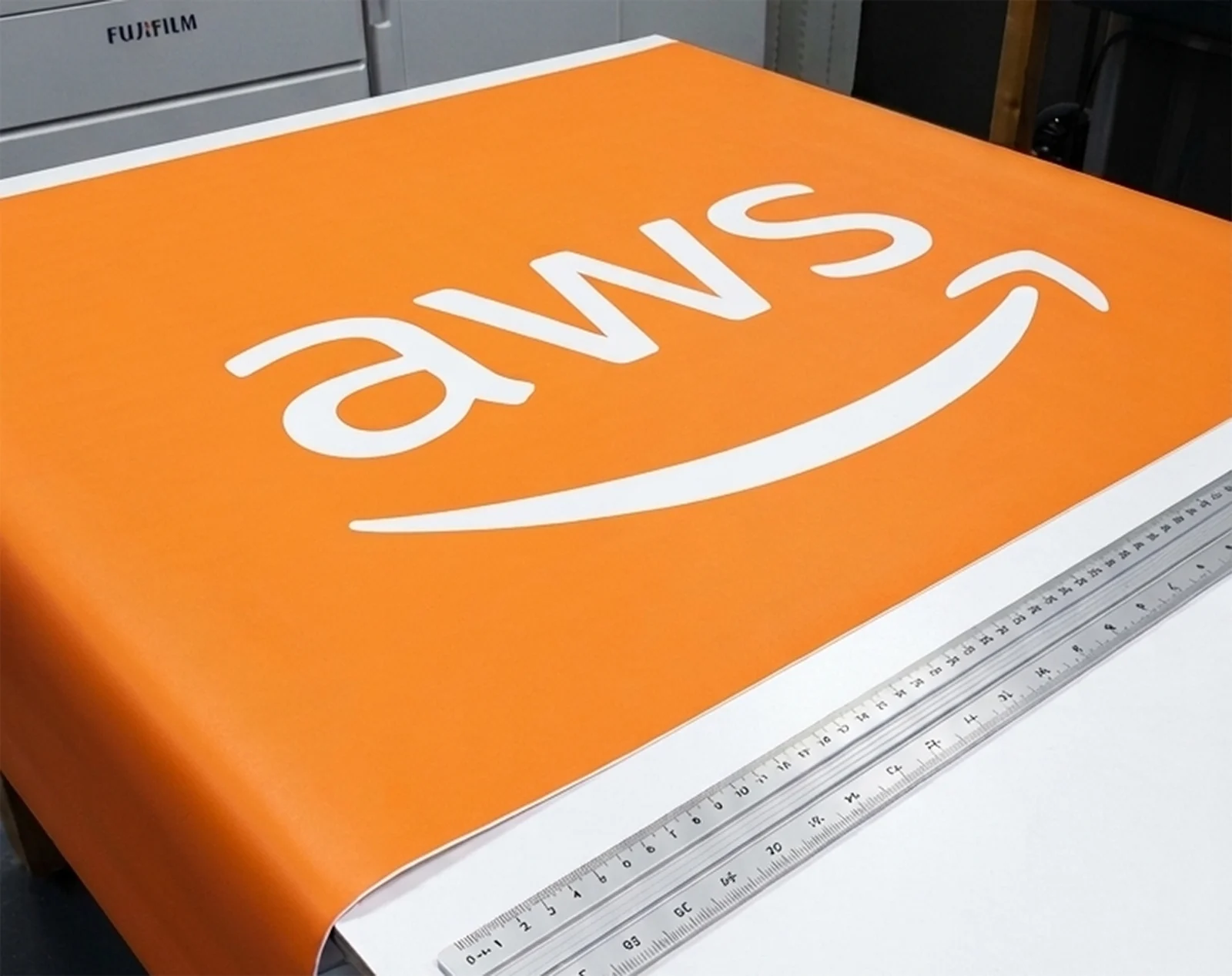 Orange printed tablecloth with a white AWS logo, laid out on the trimming table next to a steel rule