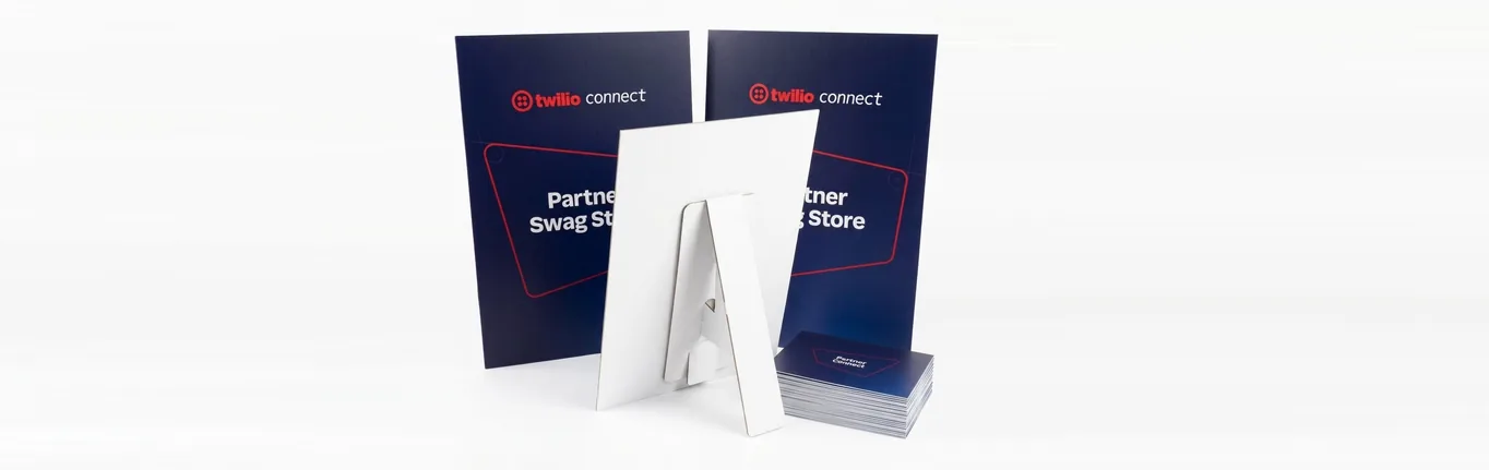 Two navy A3 Twilio Connect Partner Swag Store strut cards standing on a white surface, the white easel strut visible on the back of the front card, beside a stack of Partner Connect cue cards