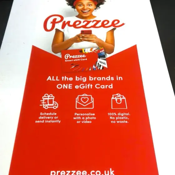 Red Prezzee gift card roller banner graphic laid flat on the bench before assembly
