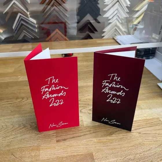 Two red Fashion Awards 2022 invitation booklets standing on a wooden table