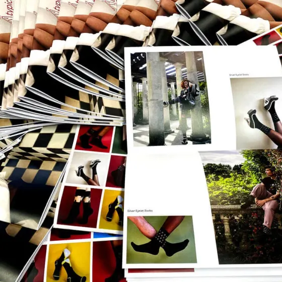 Fanned stack of Atypical AW22 lookbooks with an open copy showing model photography