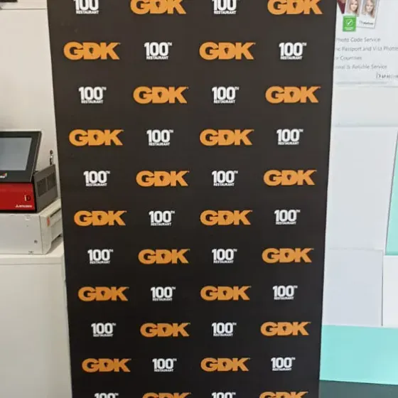 Roller banner printed with a repeating GDK 100th Restaurant pattern, standing in the print room
