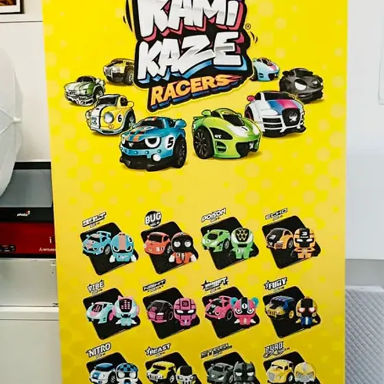 Yellow Kamikaze Racers roller banner covered in toy car illustrations, standing in the print room