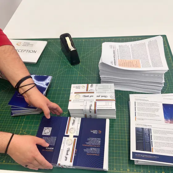 Two hands collating printed conference packs on a green cutting mat, stacks of paper alongside