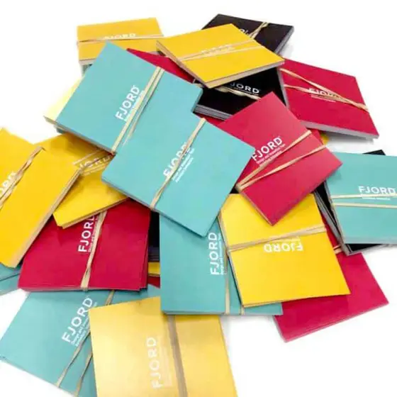 A pile of folded cards in teal, yellow, pink and black, each with a gold foil rule and logo