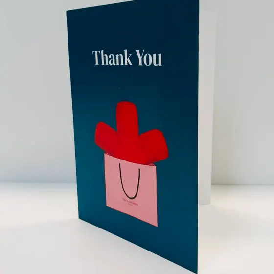 A folded thank-you card standing upright beside its white envelope, printed on dark blue board