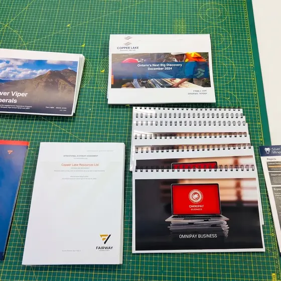 Printed investor documents laid out on a green cutting mat, bound reports and loose sheets together