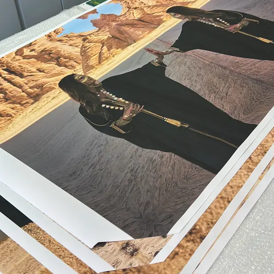 Large format photographic prints stacked face-up on the bench, the top sheet showing a desert landscape