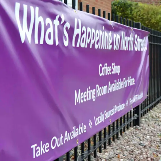 A purple PVC banner with eyelets, cable-tied to metal railings outside a brick building