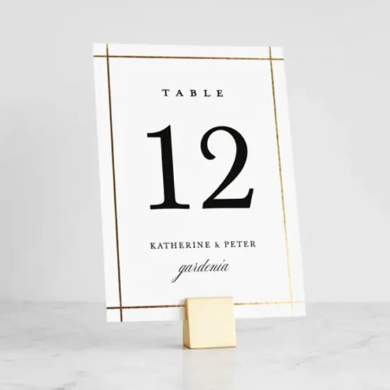 A table number card with a gold border, standing in a small wooden block on a marble surface