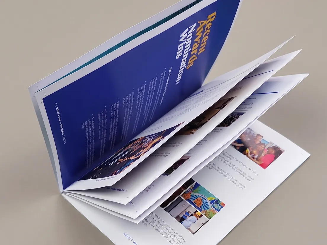 Landscape saddle stitched booklet standing open on a desk, showing the two wire stitches in the centre spread