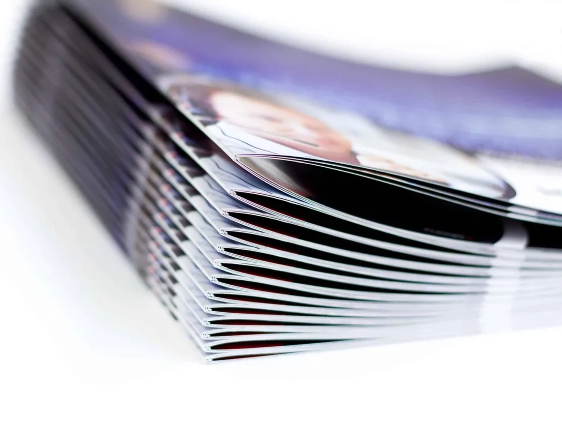 Stack of saddle stitched brochures with gloss covers fanned open at the spine edge