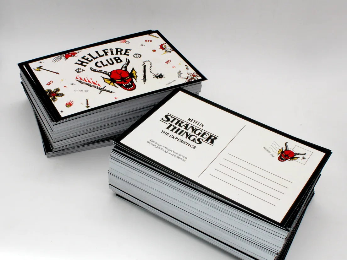 Two stacks of Stranger Things Experience event postcards, printed both sides with a black edge-to-edge border