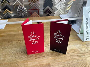 Two red Fashion Awards 2022 invitation booklets standing on a wooden table