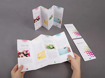 Two hands opening out a concertina-folded leaflet across several printed panels