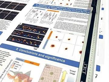 Close-up of an academic research poster on the printer bed, showing dense charts, heat maps and small-point body text