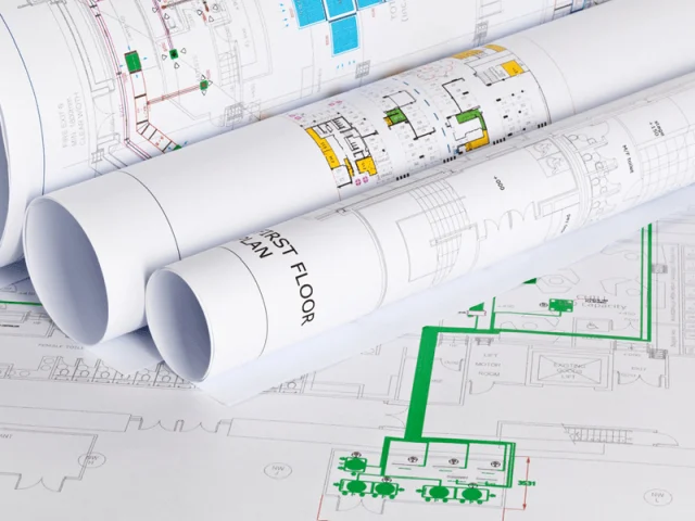 Rolled architectural floor-plan drawings lying on a desk over more printed plans