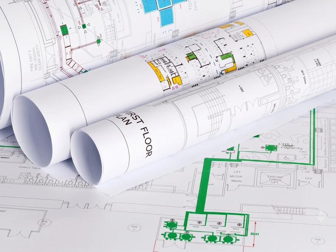 Rolled architectural plans lying on printed floor-plan drawings, showing large format CAD output