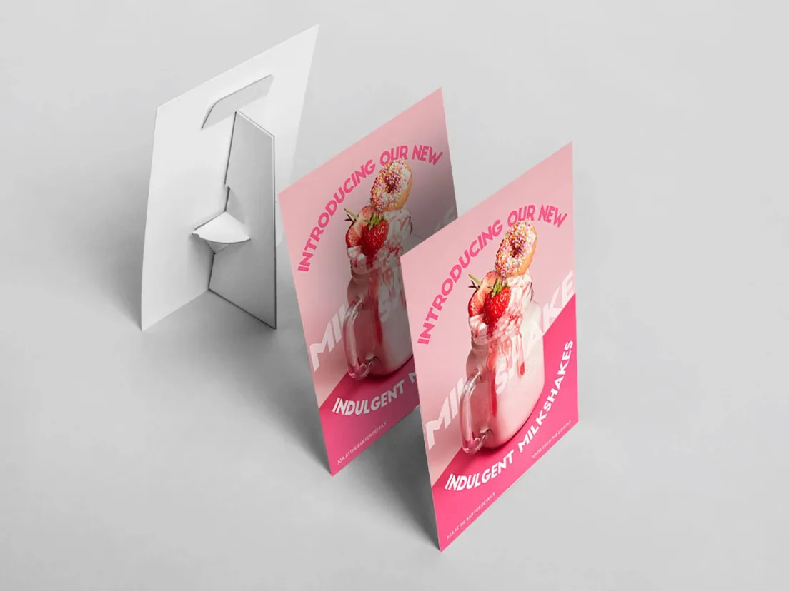 Two pink milkshake promotion strut cards standing on a counter, with a third card turned to show the fold-out strut on the back