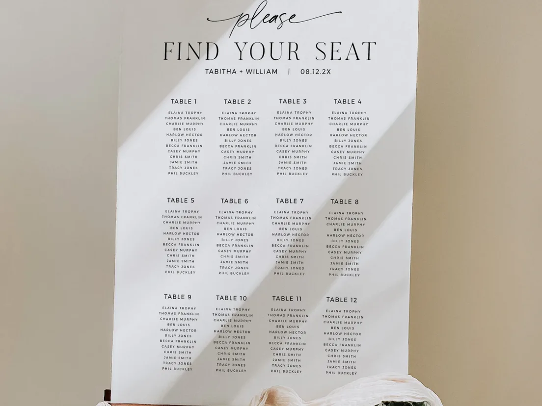 Portrait seating plan headed Find Your Seat, propped against a wall with foliage at its base