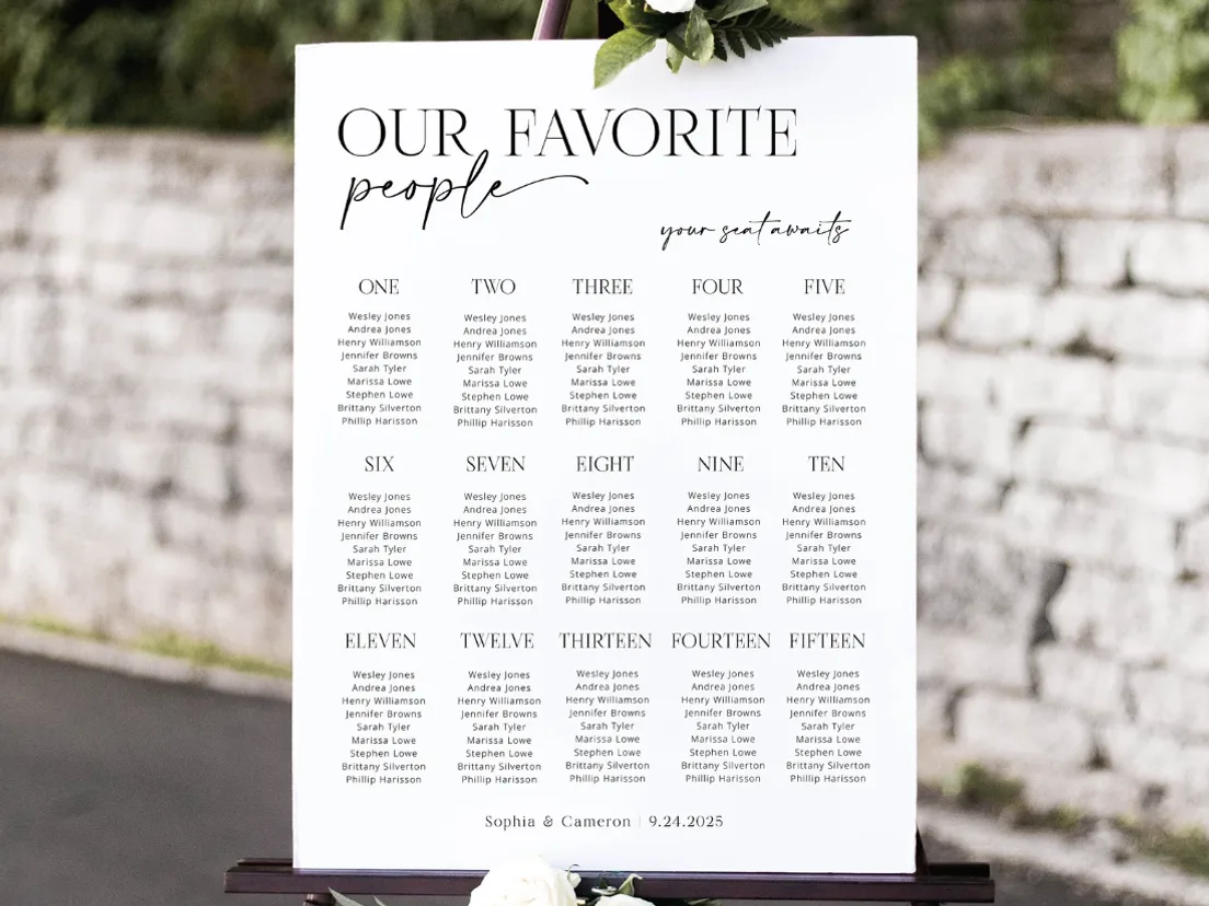 Seating plan headed Our Favorite People on a black easel against a stone wall, flowers at the base